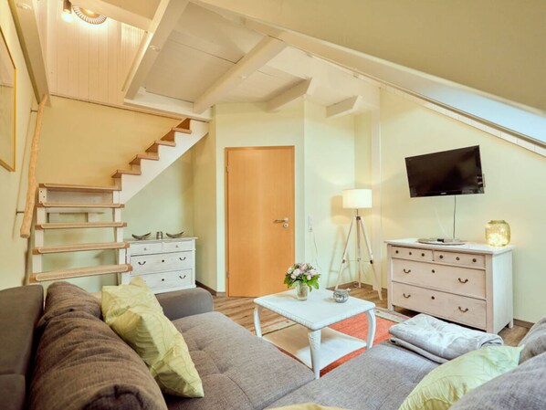 Un salon chaleureux avec un escalier, un téléviseur à écran plat, une table basse blanche et un canapé.