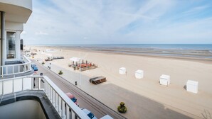 A beach view from a balcony with a clear sky, a sandy beach, and a few beach umbrellas. - Apartment on Belgian Coast With Sea View (Koksijde)