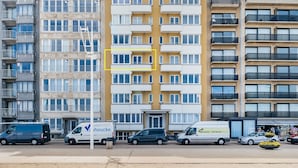 A multi-story residential building with balconies, a central entrance, and a parking area with several vehicles. - Apartment on Belgian Coast With Sea View (Koksijde)
