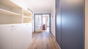 A hallway with white cabinets, a wooden floor, and a door leading to a room with a pink sofa. - Apartment on Belgian Coast With Sea View (Koksijde)