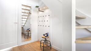 A modern hallway with a wooden floor, a staircase, and a shoe rack with shoes on stools.