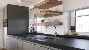 A modern kitchen with a black countertop, stainless steel sink, and wooden shelves above the counter.