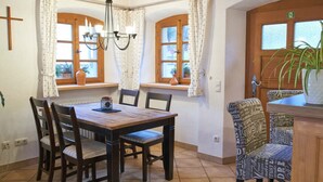 A dining area with a wooden table and chairs, two windows with curtains, a chandelier, and a potted plant. - Posthof Holiday Guesthouse (Waldmuenchen)