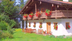 A traditional chalet with a balcony adorned with red flowers, wooden benches, and a small table with umbrellas. - Posthof Holiday Guesthouse (Waldmuenchen)