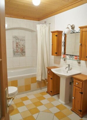 A bathroom with a checkered floor, a bathtub, a toilet, wooden cabinets, and a sink.