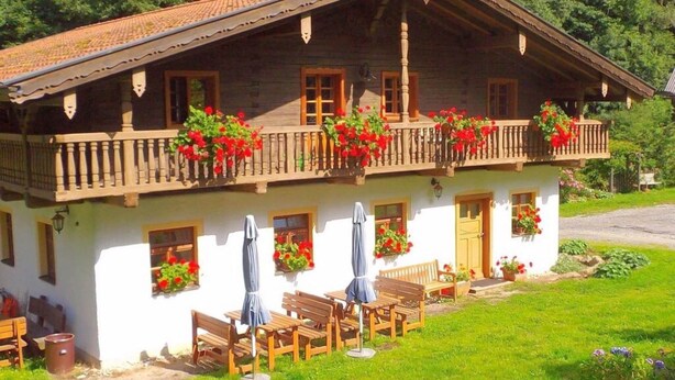 A traditional chalet with a balcony adorned with red flowers, wooden furniture, and a garden area. - Posthof Holiday Guesthouse (Waldmuenchen)