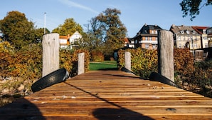Een houten vlonder die leidt naar een woongebied met huizen en bomen.