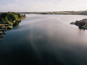 An aerial view of a calm lake with docked boats and a small building on the right.