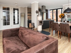 A modern living room with a brown sofa, a dining area with a table and chairs, and a kitchen with a stove and cabinets. - Reethuus Nord Modern Retreat (Juist)