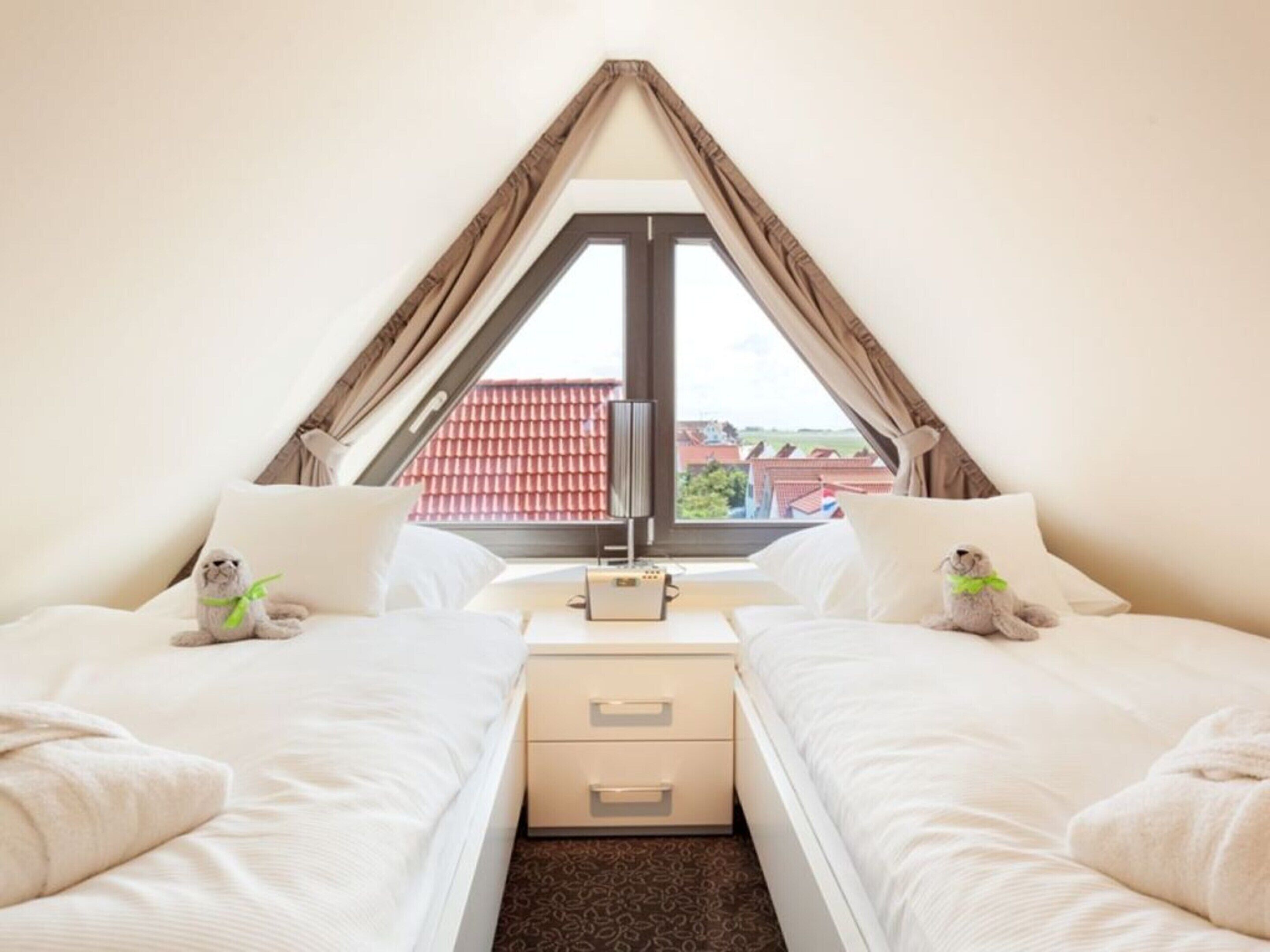 A bedroom with two beds, a nightstand, and a window with curtains.