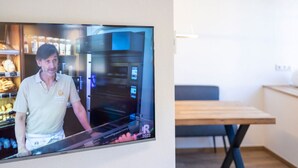 Ett modernt kök med en stor, platt tv-skärm som är monterad på väggen, ett matbord i trä och en bänk.
