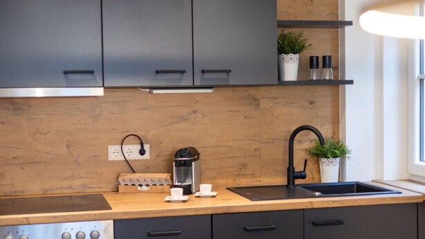 Ett modernt kök med mörka skåp, en träpanel bakom diskbänken, en kaffebryggare och en diskho.
