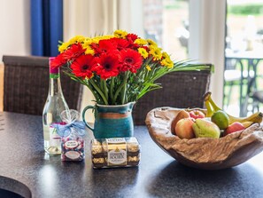 A table with a vase of red and yellow flowers, a bottle of wine, a mug, and a bowl of fruit. - Oostzeevakantie-bork (Kronsgaard)