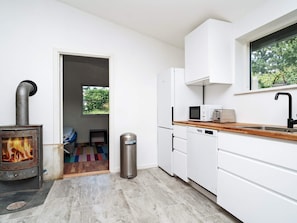 A modern kitchen with white cabinets, a wood-burning stove, a microwave, and a window with a view of greenery. - 4 Star Holiday Home in Melby (Melby)