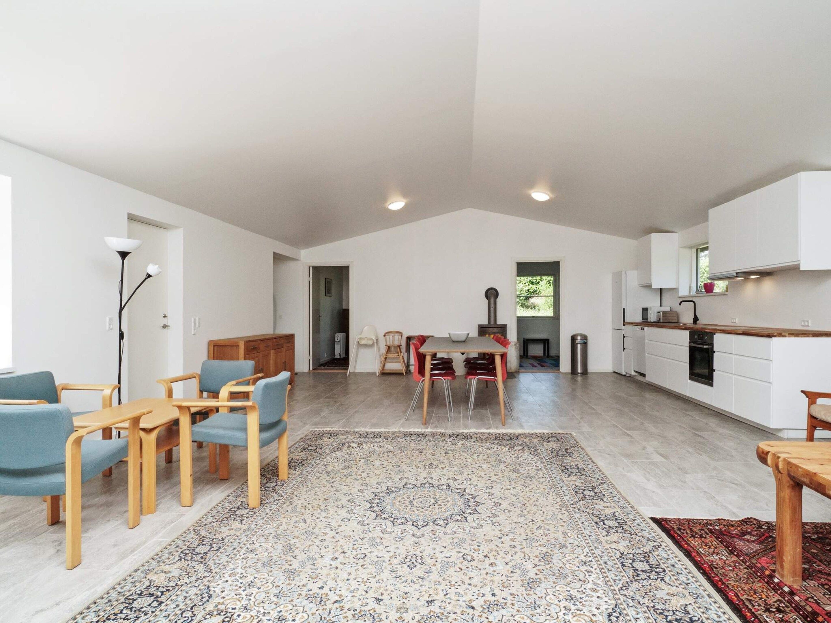 A spacious living area with a dining table, chairs, a rug, and a kitchen in the background.