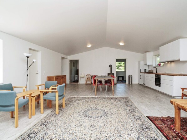 A spacious living area with a dining table, chairs, a rug, and a kitchen in the background.