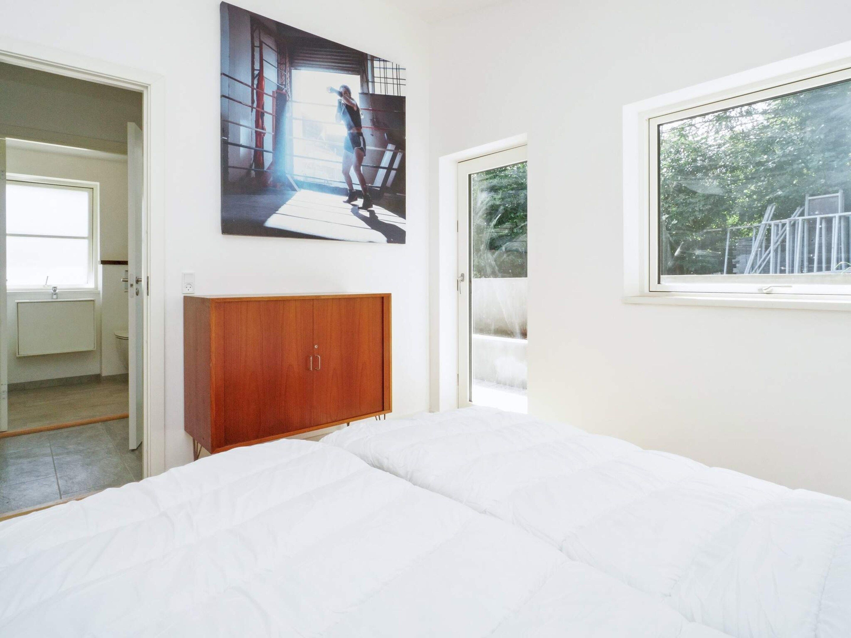 Un dormitorio con cama, armario de madera, ventana y puerta que da al baño.