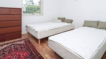 A room with two beds, a window, a wooden dresser, and a patterned rug.