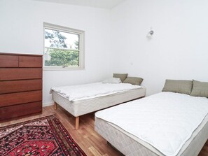 A room with two beds, a window, a wooden dresser, and a patterned rug. - 4 Star Holiday Home in Melby (Melby)