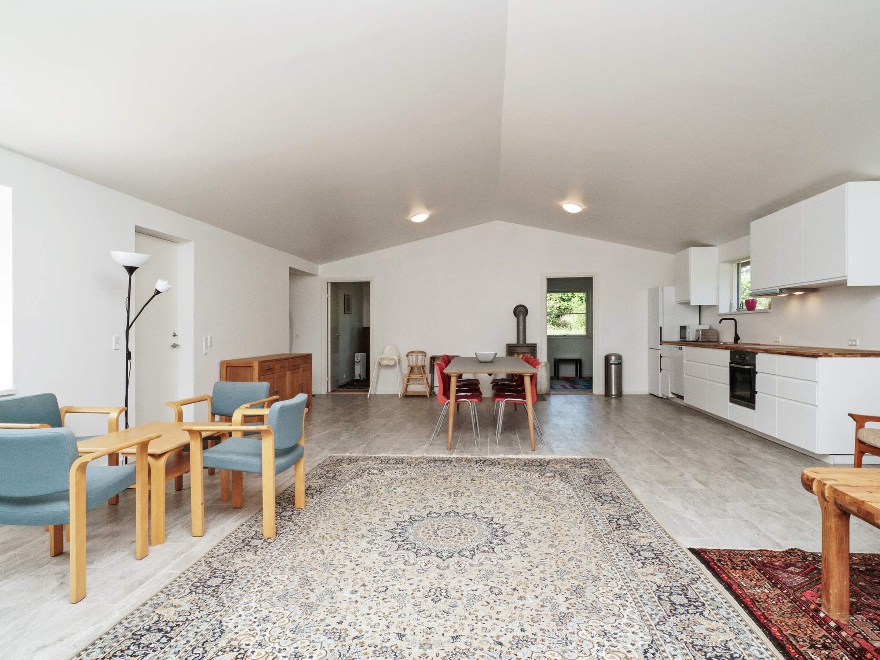 A spacious living area with a dining table, chairs, a rug, and a kitchen with white cabinets and a stove.
