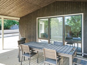 An outdoor patio with a wooden table and chairs, large windows, and a view of the outdoors. - 4 Star Holiday Home in Melby (Melby)