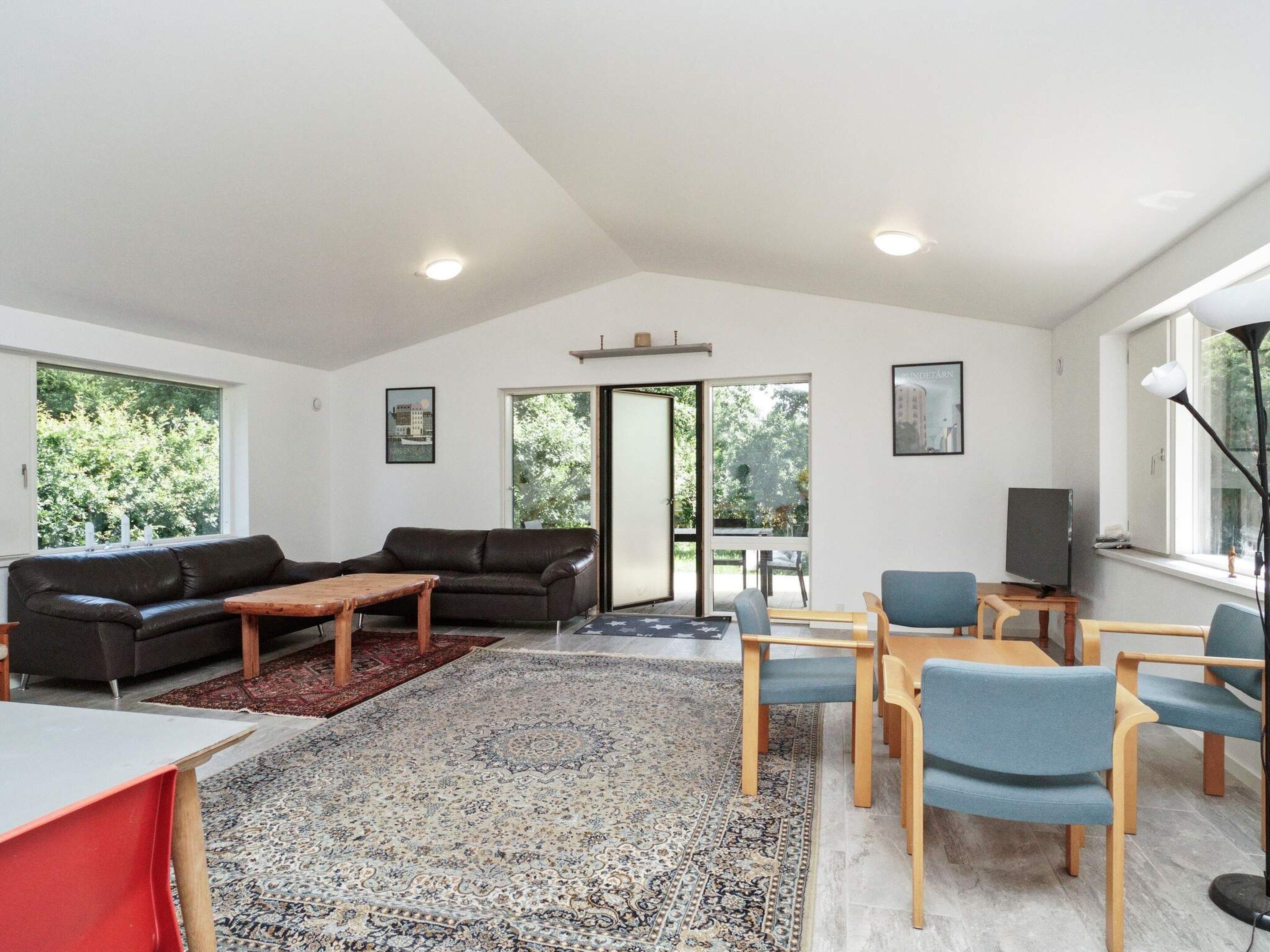 A modern living room with a sofa, coffee table, and chairs, a TV, and a large window with a view of trees.