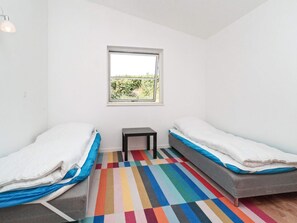 A room with two beds, a small table, a window with a view of greenery, and a colorful striped floor. - 4 Star Holiday Home in Melby (Melby)