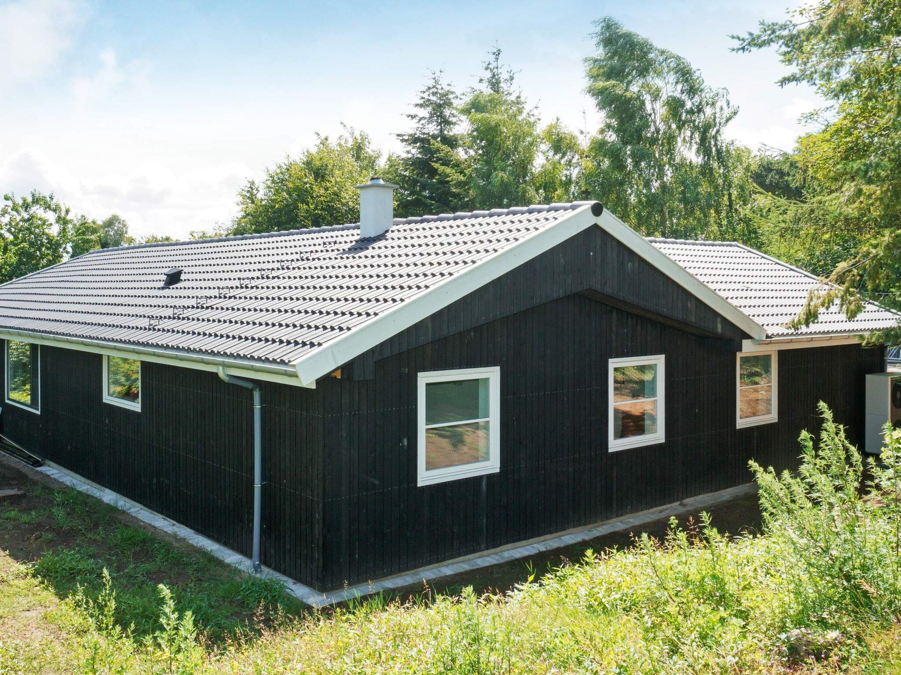 Una casa de madera negra con techo a dos aguas, dos ventanas y una chimenea.