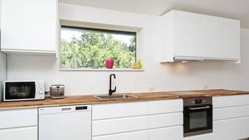 A modern kitchen with white cabinets, a wooden countertop, a built-in dishwasher, a stainless steel oven, and a window with a view of trees.