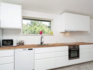 A modern kitchen with white cabinets, a wooden countertop, a built-in dishwasher, a stainless steel oven, and a window with a view of trees.