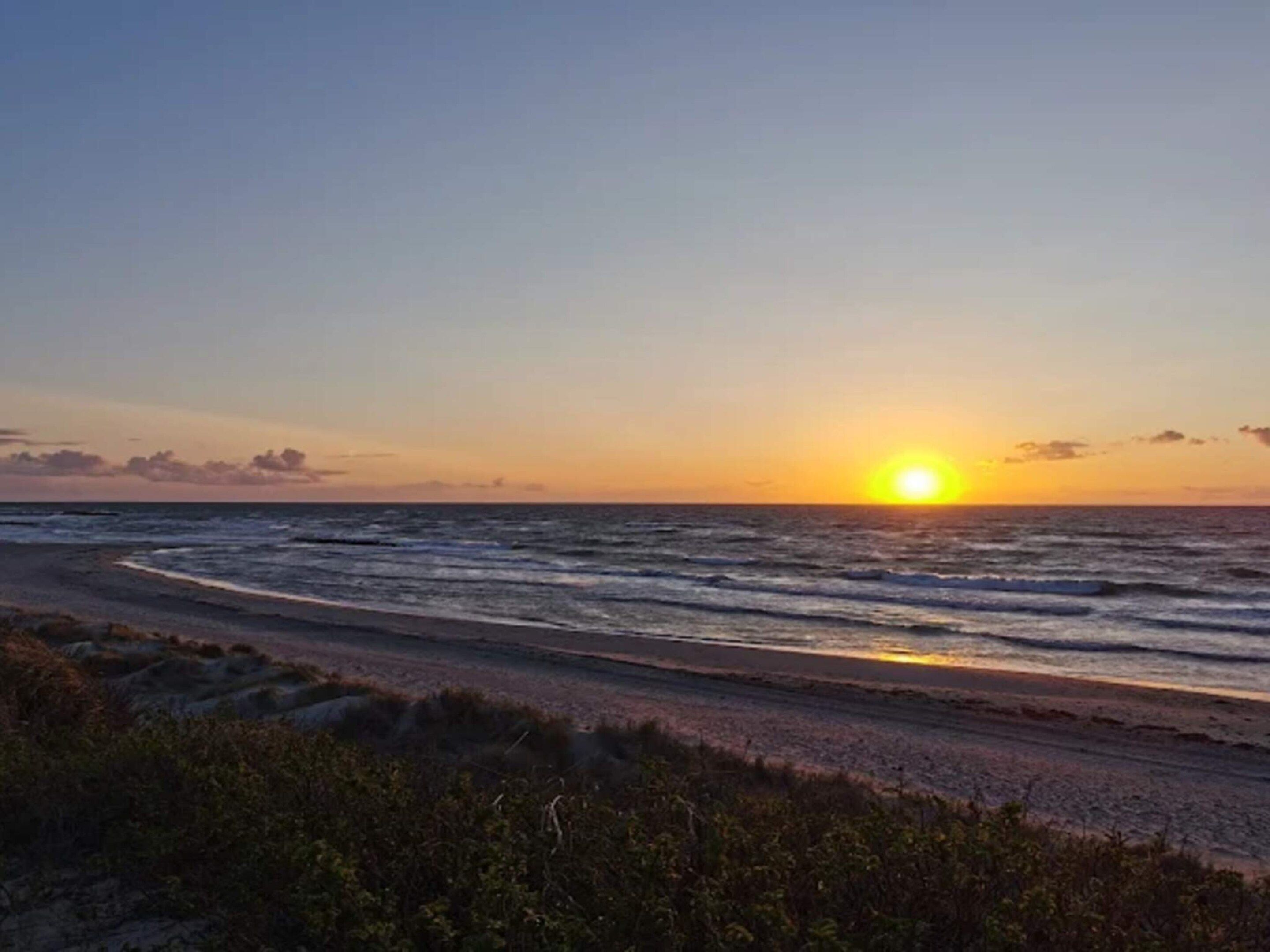 Una playa con el sol poniéndose sobre el océano.