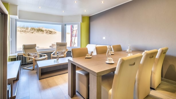 A modern dining area with a large table and comfortable seating, large windows with a view of the beach, and a clean, minimalist design. - Apartment Near Dunes With Sea View (Koksijde)