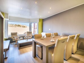 A modern dining area with a large table and comfortable seating, large windows with a view of the beach, and a clean, minimalist design. - Apartment Near Dunes With Sea View (Koksijde)
