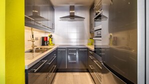 A modern kitchen with stainless steel appliances, a central island, and a bright yellow accent wall. - Apartment Near Dunes With Sea View (Koksijde)