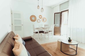 Ein modernes Wohnzimmer mit einer braunen Couch, einem Esstisch mit weißen Stühlen und einem runden Couchtisch.
