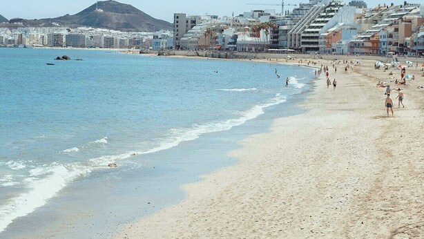 A beach with a cityscape in the background, including buildings and a hill.