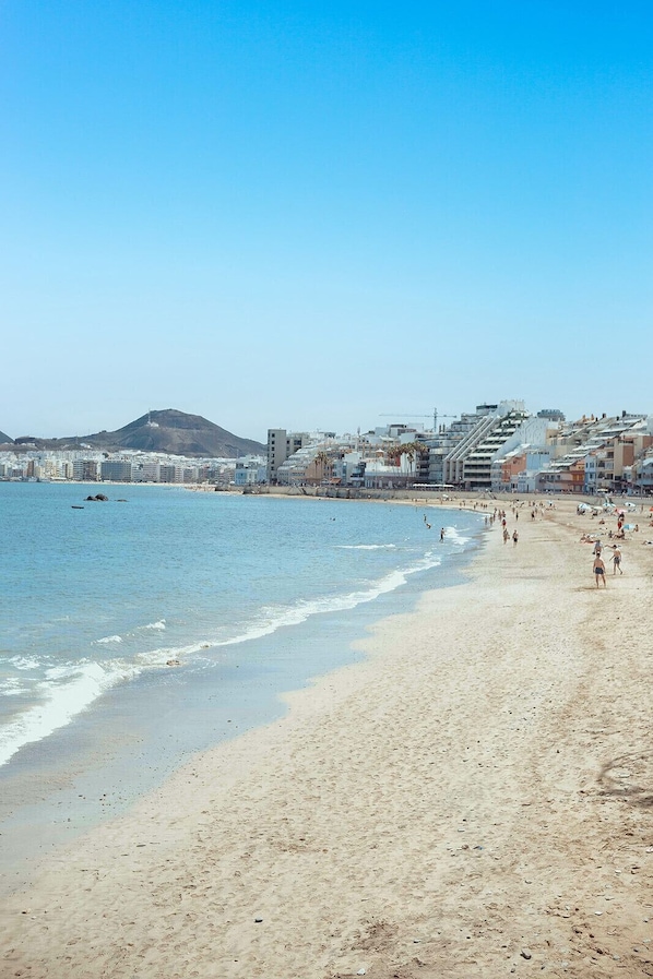Ein Strand mit einer Stadtlandschaft im Hintergrund, darunter Gebäude und ein Hügel.