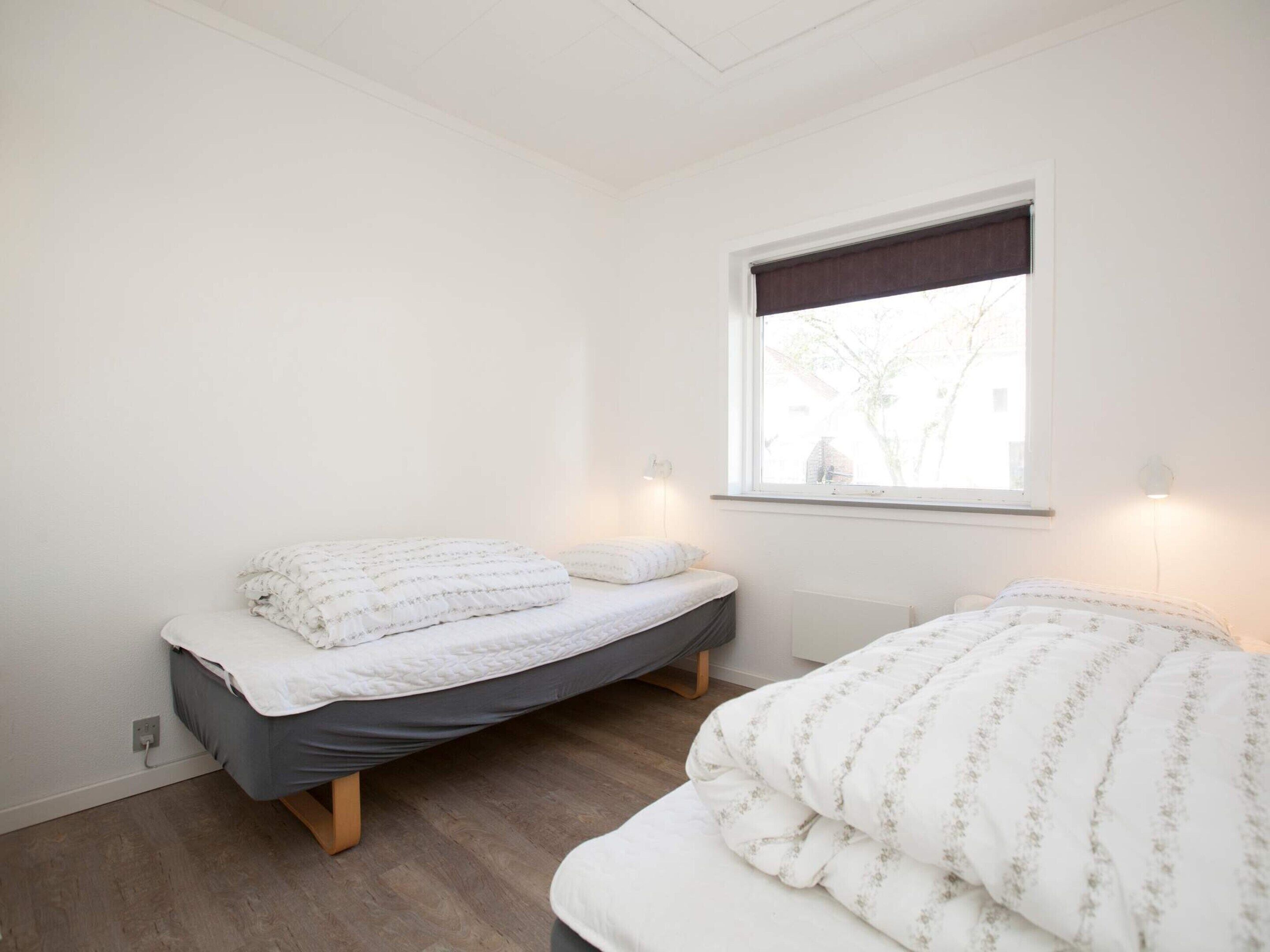 A bedroom with two single beds, a window with a view, and a wall-mounted light fixture.