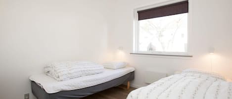 A bedroom with two single beds, a window with a view, and a wall-mounted light fixture.