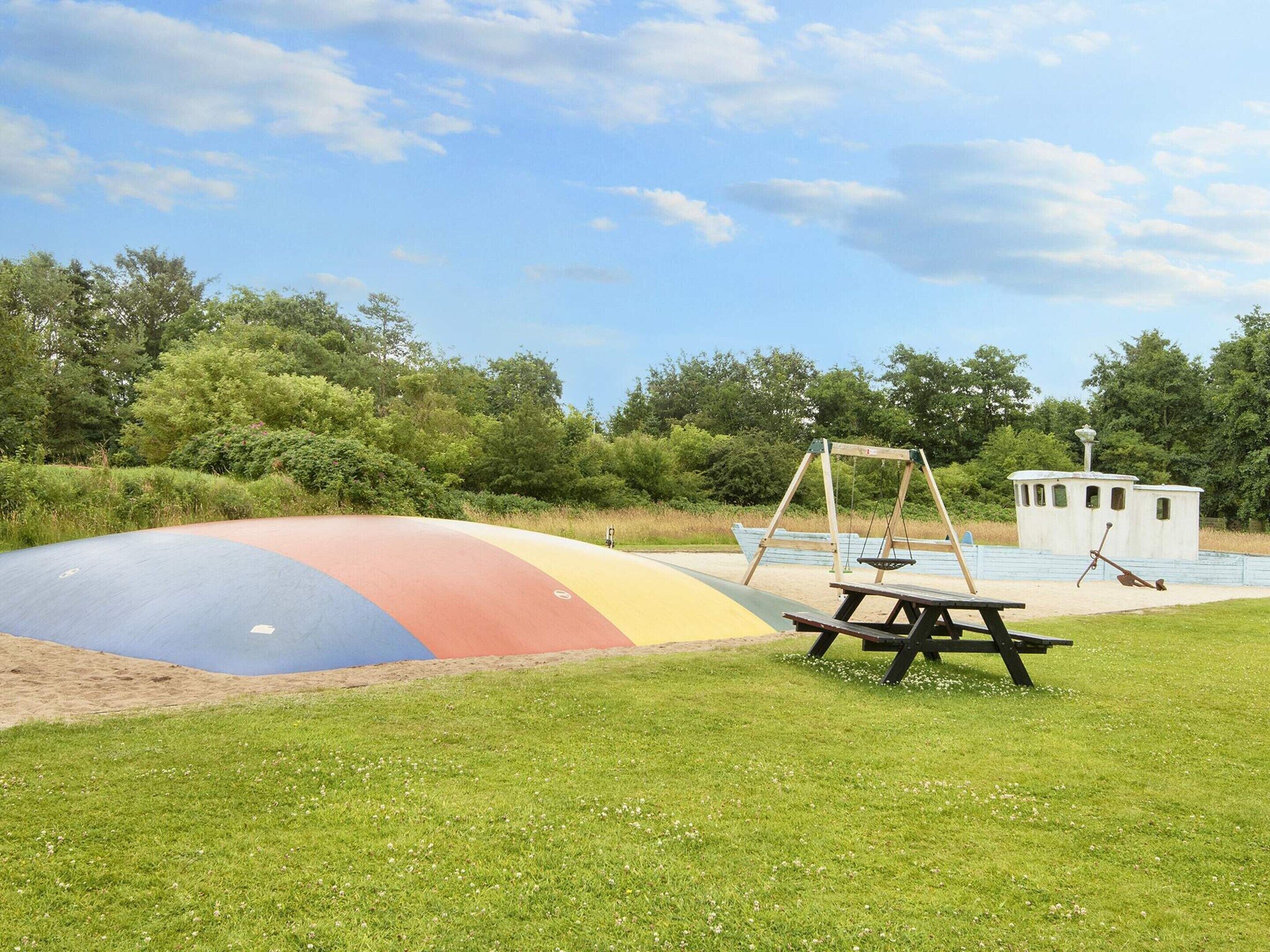 Ein Spielplatz mit einer bunten Rutsche, Schaukeln und einem Picknicktisch.