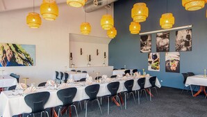 Une salle de conférence avec des tables disposées pour une réunion, des lampes suspendues jaunes et des œuvres d’art mural.