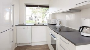 Une cuisine moderne avec des meubles blancs, un plan de travail noir, un four encastré et une fenêtre donnant sur un paysage verdoyant.