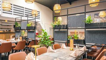 A modern restaurant with long tables, orange chairs, and hanging wicker lamps.
