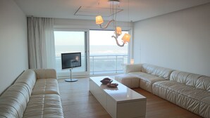 A modern living room with a large window, a flat-screen TV, and two sofas. - Romantic Coastal Escape (Nieuwpoort)
