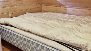 Un dormitorio con techo inclinado de madera, colchón con cubierta estampada y dosel a cuadros.
