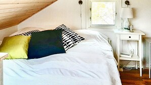 Une chambre avec un plafond en pente, un lit avec une literie blanche, une table de chevet avec une lampe et une fenêtre donnant sur un beau paysage.