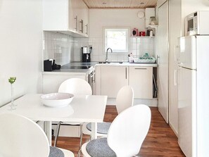 A modern kitchen with white cabinetry, a dining table with chairs, and a refrigerator.