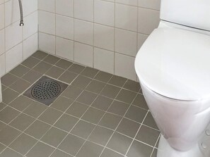 Een badkamer met een wit toilet, een afvoerputje in de vloer en witte tegels.