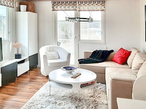 Een moderne woonkamer met een witte bank, een witte fauteuil, een ronde salontafel en een wit tapijt.