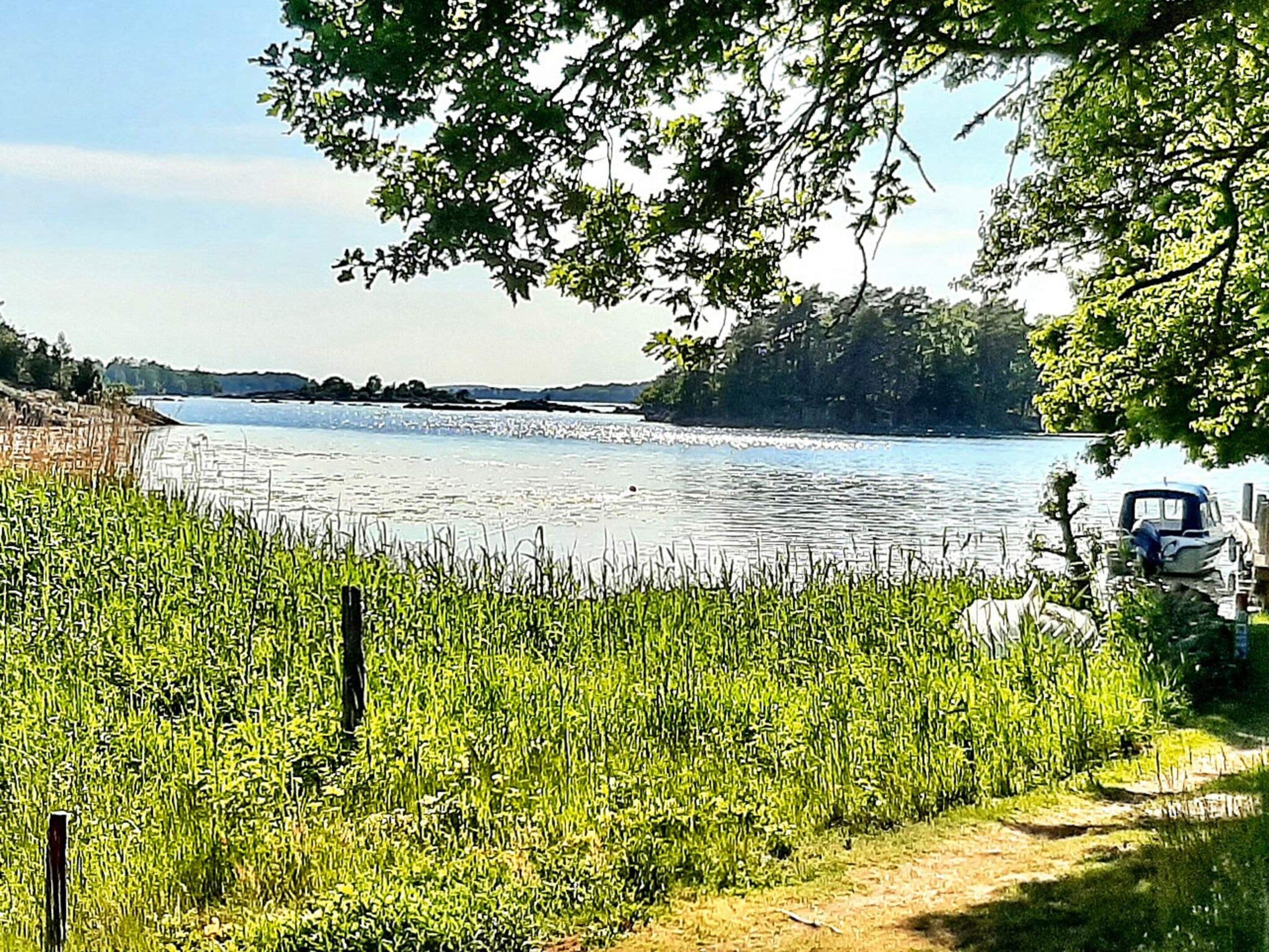 A lakeside view with a boat docked on the right, surrounded by greenery and a clear sky.